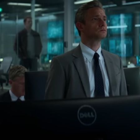 Martin Freeman is wearing a grey suit, looking at the big screen.